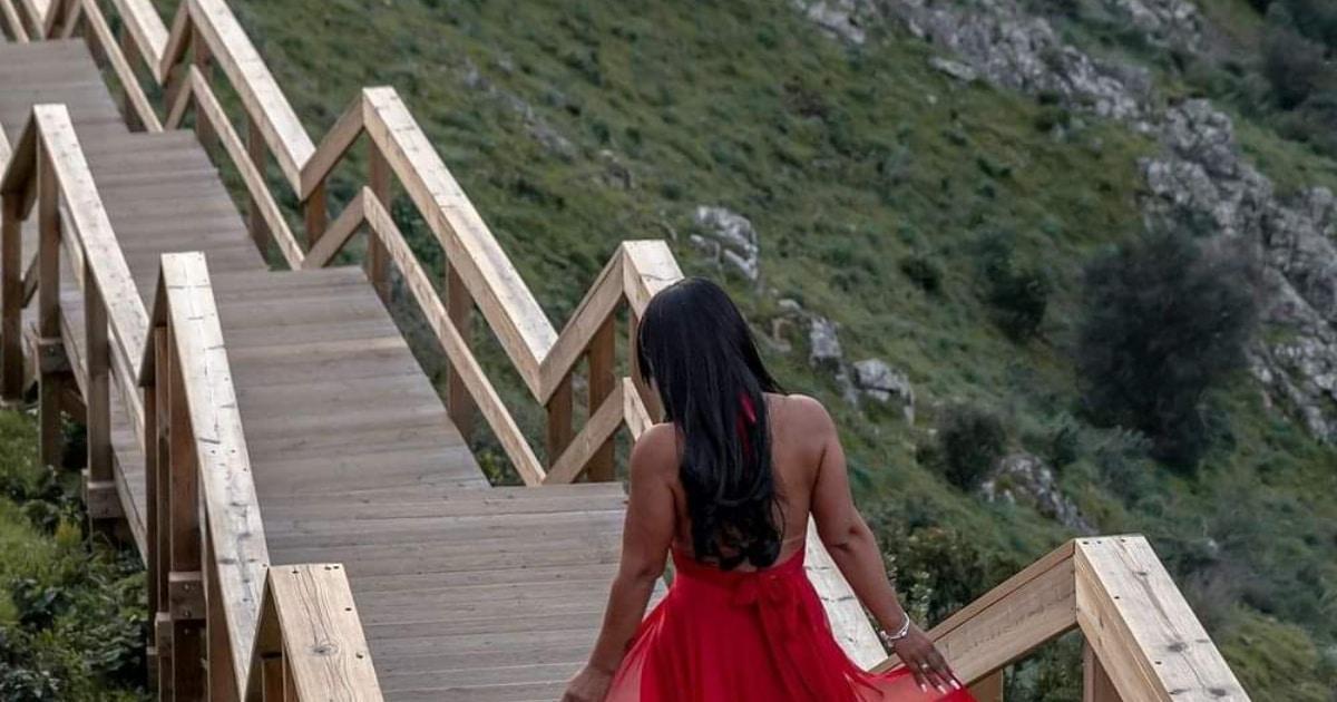 Mulher em vestido vermelho numa ponte de madeira.