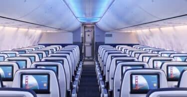 Interior de avião com assentos e ecrãs.
